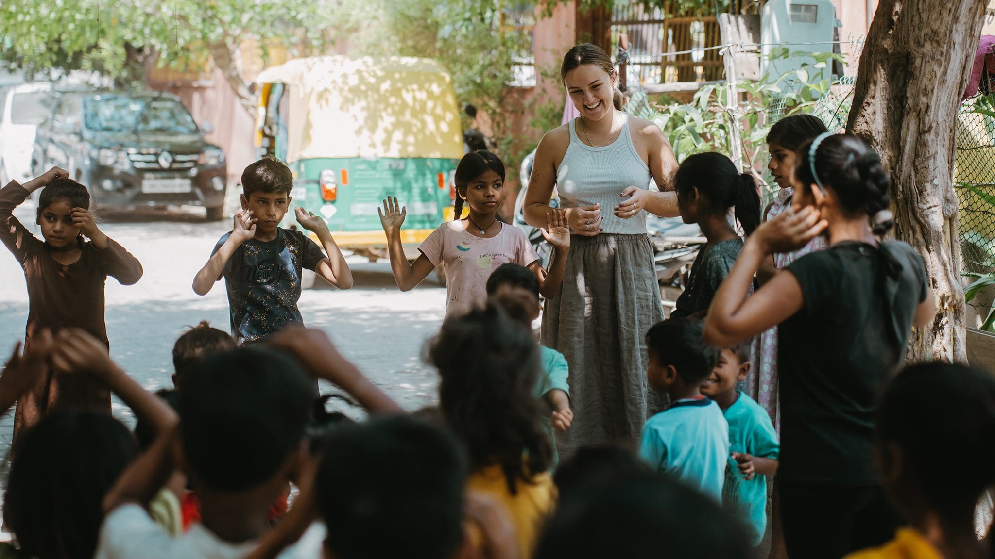 Children enjoying outdoor community activity with facilitator amid sunny, green urban setting.