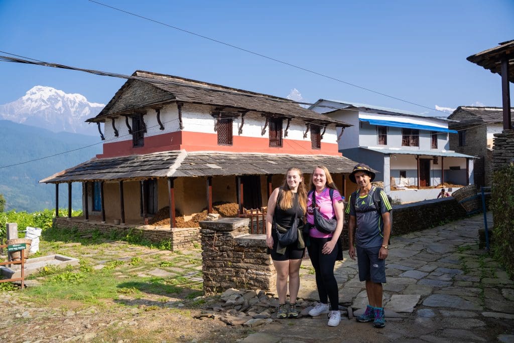 Himalayan village with trekkers, traditional houses, lush greenery and majestic snow-capped mountains